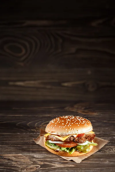 Hambúrguer de queijo com carne grelhada, queijo, tomate, sobre papel artesanal sobre superfície de madeira. Modelo de fast food . — Fotografia de Stock