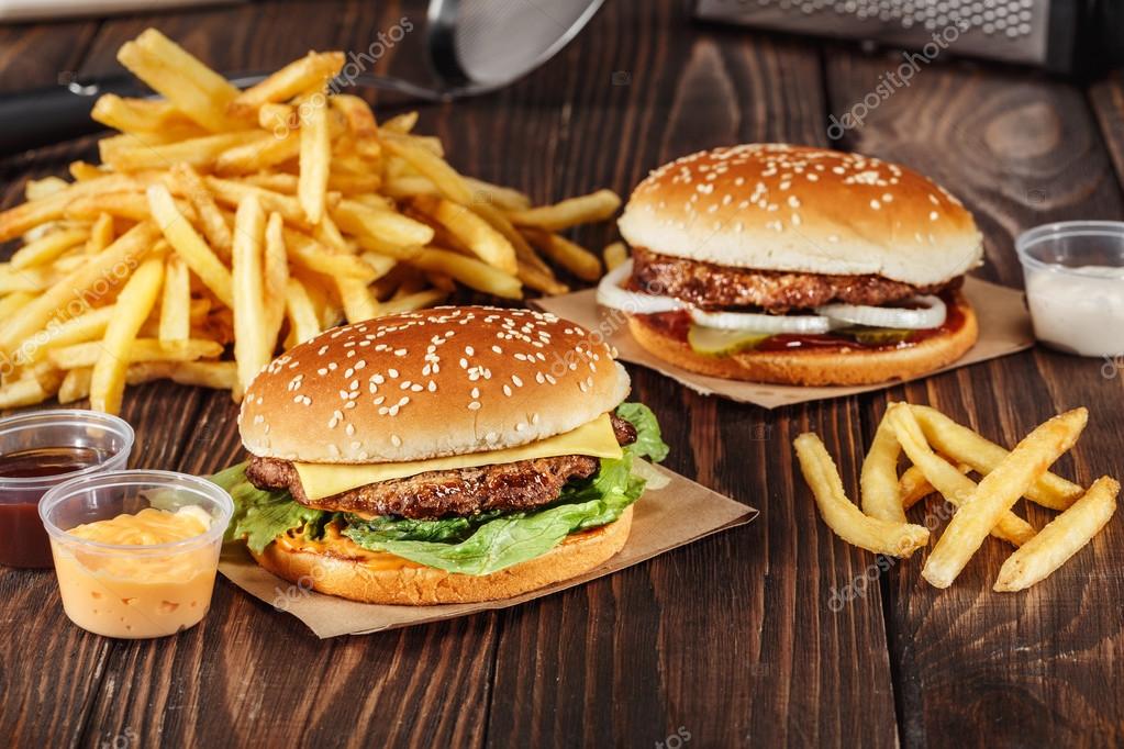 Two burgers with grilled meat with french fries on craft paper on wooden surface in kitchen. Fast food template. real photo