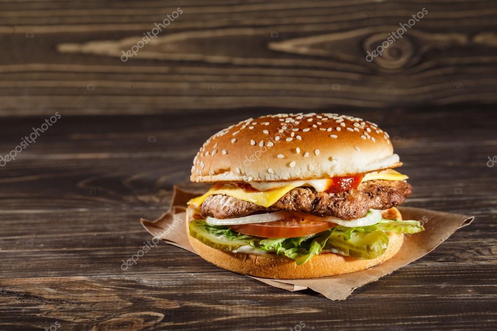 Cheese burger with grilled meat, cheese, tomato, on craft paper on wooden surface. Fast food template.