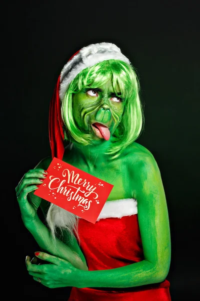 Closeup portret van jong meisje in rood Kerstman met greasepaint grinch gezicht kunst. Nieuwjaar cadeau auto met wensen vrolijk kerstfeest. Negatieve emotie gelaatsuitdrukking gevoel — Stockfoto