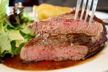 Biftek çatalında dilimlenmiş, beyaz tabakta kahverengi soslu sığır eti. Orta seviye olgun. Gıda konsepti.