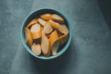 Haşlanmış domuz sosisi dilimlenmiş ve yenmeye hazır mavi kasede servis ediliyor. Üst görünüm