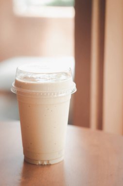 Sütlü kahve smoothie 'yi ahşap masada plastik bardakta kapat.