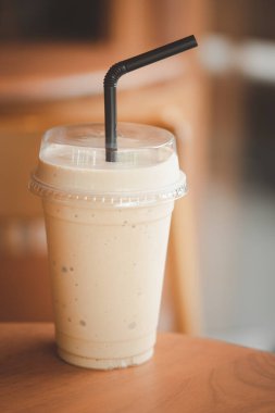 Ahşap masada plastik bir bardak buzlu içecek.