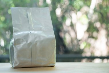 Beyaz parlak folyolu kahve poşeti doğanın arka planında, masanın üzerinde. Boş ambalaj alüminyum folyo kesesi