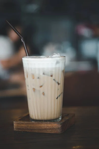 ミルクフォームと木のテーブルの上のわらとアイスコーヒーカプチーノのガラス — ストック写真