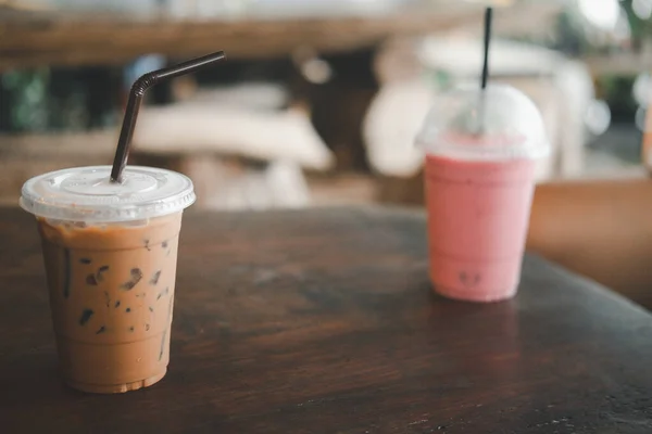 Iced coffee mocha in plastic take away cup on wooden table in cafe and blurred of strawberry smoothie. Selective focus in mocha