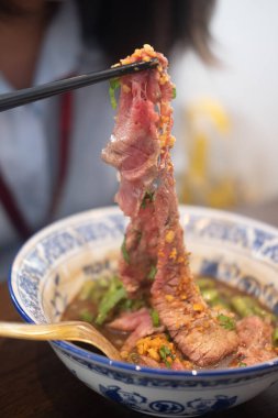 Tayland erişte kasesindeki çubukları kullanarak Wagyu bifteğinden bir dilim aşırmak. Seçici odak