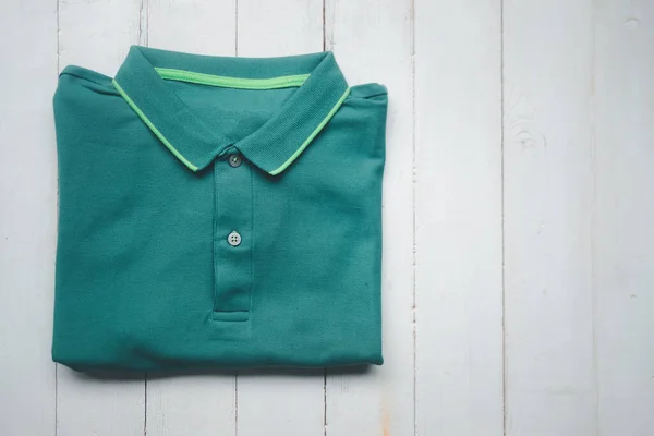 Folded green polo shirt on grey wooden desk. Top view