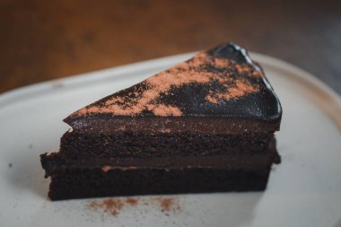 Çikolata tozuyla süslenmiş beyaz tabakta çikolatalı pastanın üç dilimini kapat.