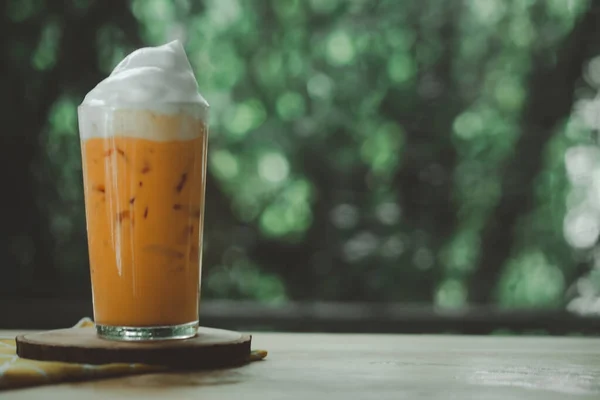 A glass of Thai milk tea with milk foam on top arranged on nature background