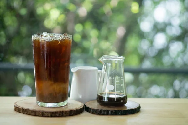 A glass of cold coffee and ice served with cream in small jar. Cold summer drink on a wooden table