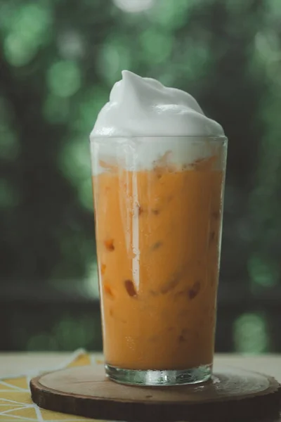 A glass of Thai milk tea with milk foam on top arranged on nature background