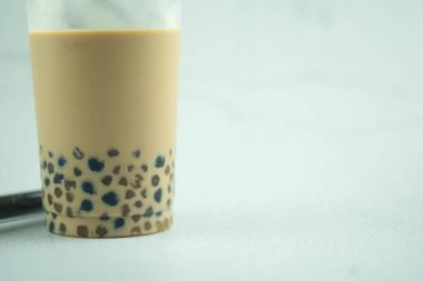 Beyaz arka planda plastik bardakta buzlu sütlü çay ve köpüklü boba.