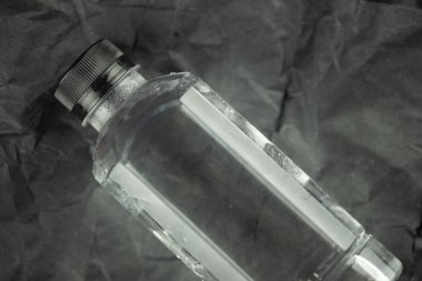 Plastik şişe soğuk su siyah buruşuk kağıt arka planda
