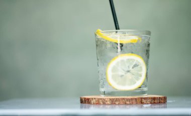Bir bardak buz ve su, bir dilim limonla süslenmiş, ahşap tabakta siyah kamışla.