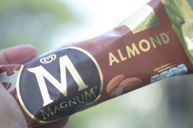 Samut Prakan, Tayland - 15 Ocak 2021: Doğanın soyut bulanık arka planına sahip badem aromalı Magnum dondurması tutarken çekilmiş bir fotoğraf.