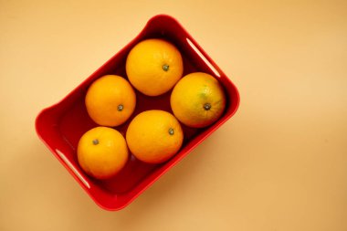 Sarı arka planda kırmızı kutuda taze portakallar. Üst görünüm
