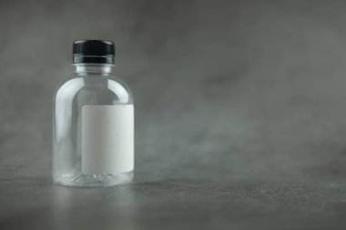 Siyah kapaklı boş plastik şişe ve siyah arka planda boş etiket. Tasarımınız için paket kavramı