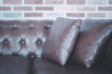 Oturma odasındaki tuğla duvarda kahverengi deri kanepe ve yastıklar.