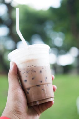 Yeşil arka planda plastik bardak buzlu kahveyi tutan adam, buzlu kahve.