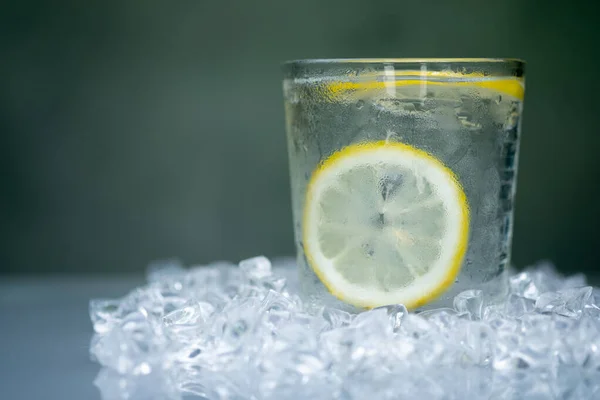 A glass of cool water with slice lemon inside served on a ice cubes artificial crystal piece