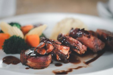 Pişmiş sebzede servis edilen domuz pastırmalı fileto.