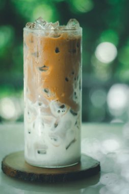 Ahşap bir masanın üzerinde buzlu kahve. İçine kahve dökülüyor. İçkinin dokusunu ve ferahlatıcı görünüşünü gösteriyor. Büyük bardakta buzlu kahve..