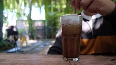 Buzlu Mocha kahvesini kadehle karıştıran genç adam çekim yapıyor.