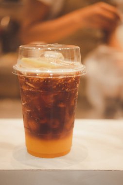 El yapımı soda ve portakal suyuyla karıştırılmış plastik bir bardak espresso ve bulanık arka planda portakal dilimi..