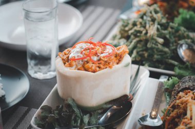 Karides, istiridye, yengeç, baharatlı Tayland yemeği ve köri ezmesi. Ho Mok Talay adlı Tayland yemeği beyaz hindistan cevizi kabuğunda servis edilir.