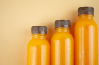 Plastik şişedeki üç portakal suyunu turuncu arkaplana yaklaştır ve boşluğu kopyala