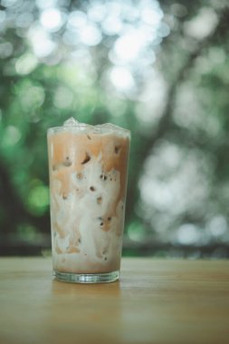 Tahta bir sehpada buzlu kahve ve üzerine taze süt dökülüyor. Doğal bir geçmişi olan ferahlatıcı içeceği gösteriyor.