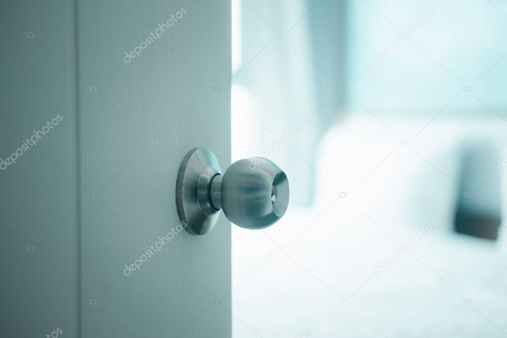 White door with handle opening through bedroom. Door half opened on blurred bedroom background. Selective focus.