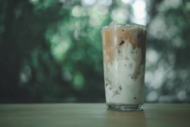 Tahta bir sehpada buzlu kahve ve üzerine taze süt dökülüyor. Doğal bir geçmişi olan ferahlatıcı içeceği gösteriyor.