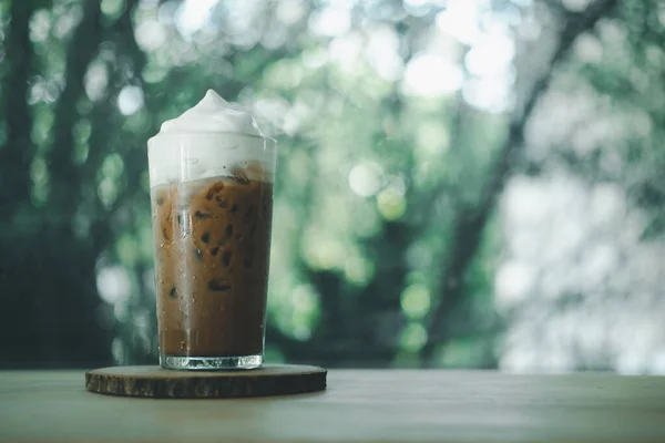 A glass of iced mocha coffee with milk foam, espresso mixed with chocolate or cocoa topped with milk foam on table at coffee cafe.