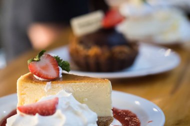 Krem şantili bir dilim cheesecake ve beyaz tabakta çilekli, seçici bir odak