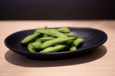 Haşlanmış Edamame, Japon restoranında kara tabakta yeşil soya fasulyesi. Aperatif konsepti