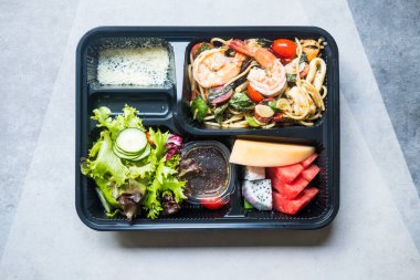 Kızarmış baharatlı spagetti soslu salata ve meyve ve beslenme çantasının üst görüntüsü.