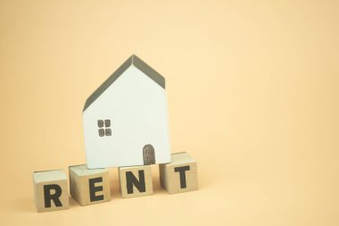Ahşap bloklar üzerinde sarı arka planlı ahşap evle birlikte RENT harfleri var..
