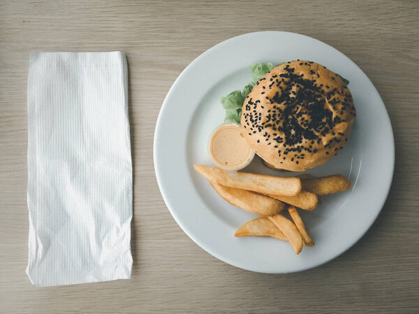 Tasty burger served with french fries on white plate place on wood table