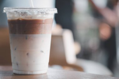 Buzlu latte kahve, en alttaki sütlü kahve. Plastik bardakta 16ons. Tahta masada.