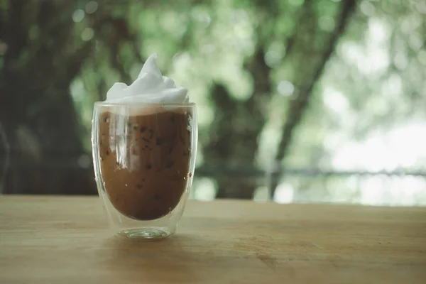 Iced mocha coffee with milk froth on top in a double-walled glass placed on wood table