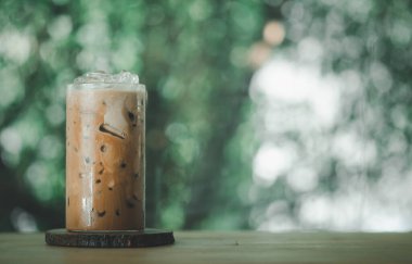 Buzlu Mocha kahvesi, üzerinde krema olan bir bardakta, ahşap bir masanın üzerinde, doğa arka planına karşı..