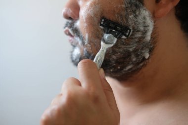 Asyalı bir adam banyoda sakalını kesiyor.