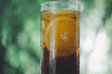 Close up a glass of sparkling soft drink with orange sliced and ice against nature background. Cold refreshing summer drink