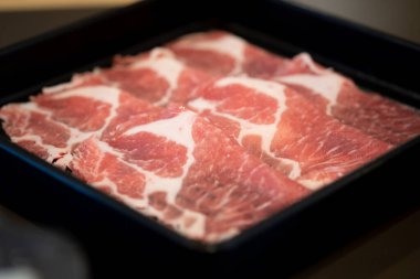 Close up of premium fresh sliced meat beef in black tray are prepared for cooking in a shabu-shabu hot pot or sukiyaki. Red raw meat with beautiful white fat texture.