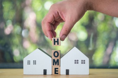 The hand puts a wooden cube with the letter H from the word HOME between two home. Banking, real estate, Property investment, home mortgage