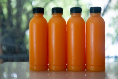Dört şişe taze portakal suyu. Arka planda siyah kapaklı.