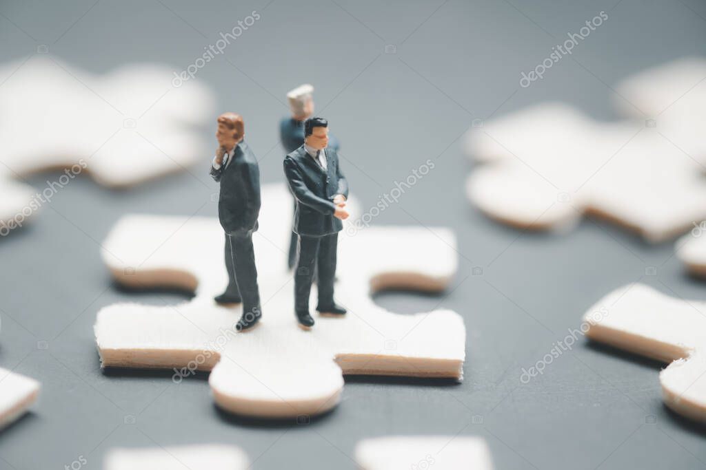 Three miniature businessman standing with their backs and standing above jigsaw puzzle piece for find common solution. Partnership concept
